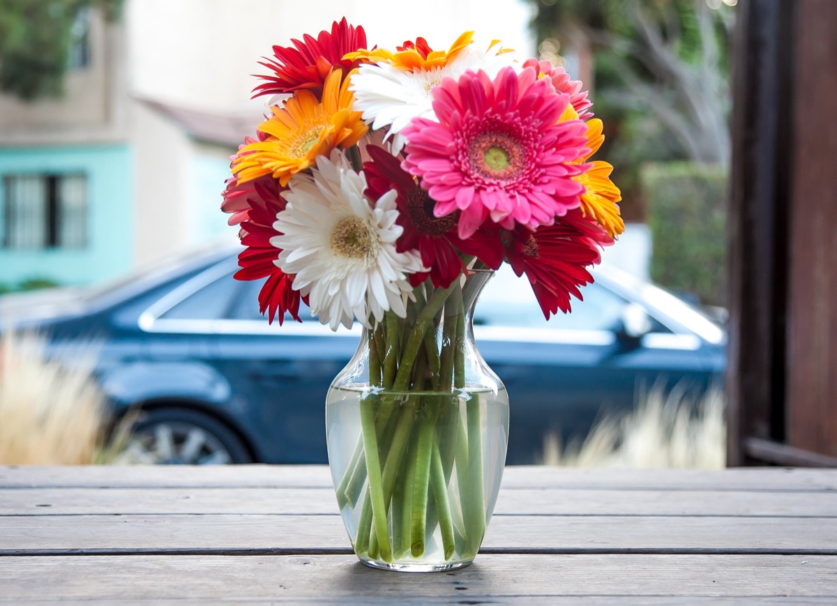 Ramo de gerberas de colores en un florero de vidrio sobre una mesa de madera.